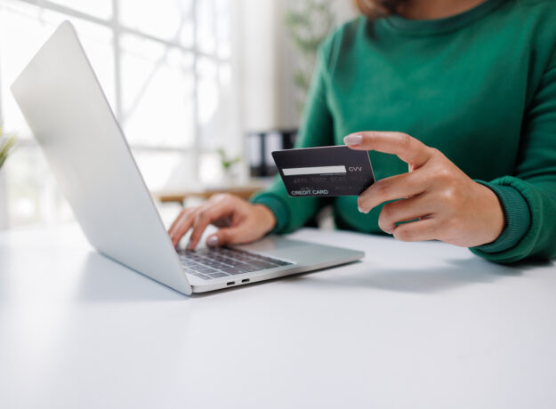 A person is engaged in online shopping, holding a credit card in one hand and typing on a laptop with the other, showcasing modern digital transaction habits.