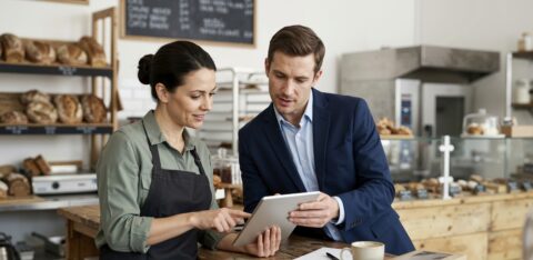 Bakery owner and financial professional discussing business finances using a tablet.