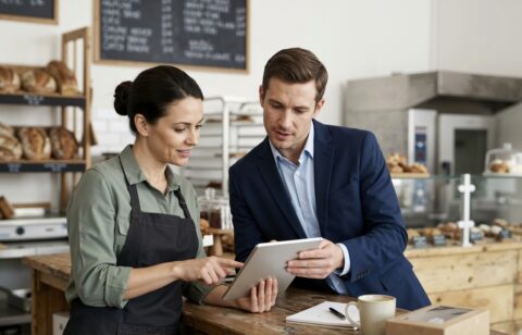 Bakery owner and financial professional discussing business finances using a tablet.