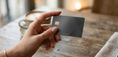 Close-up of a hand holding a credit card above a wooden table.