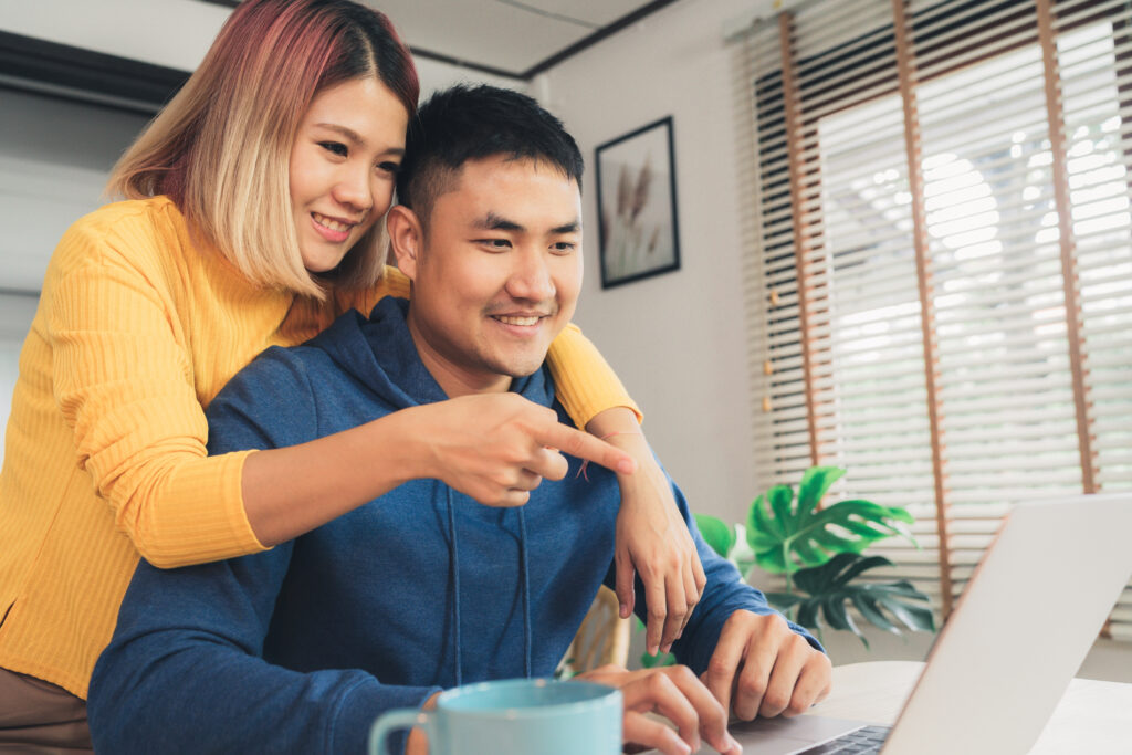 Couple smiling while looking at a laptop together at home.