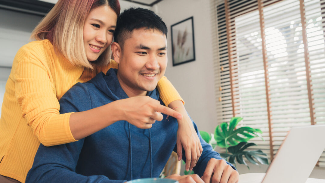 Couple smiling while looking at a laptop together at home.