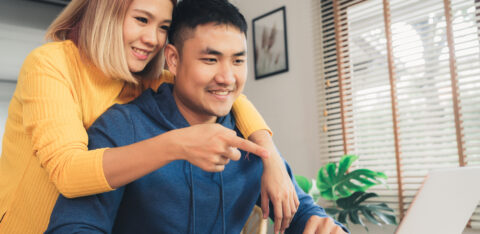 Couple smiling while looking at a laptop together at home.