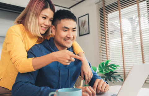 Couple smiling while looking at a laptop together at home.
