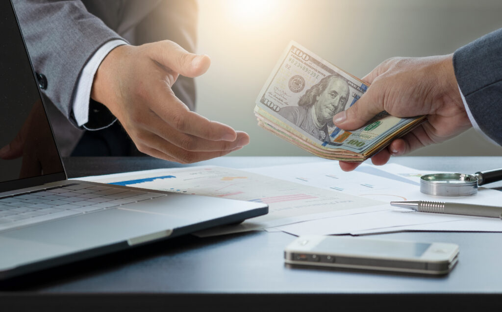 Close-up of one person handing a stack of hundred-dollar bills to another across a desk.
