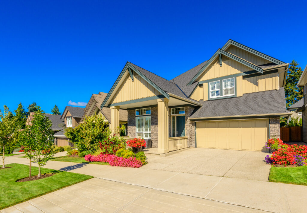 Large two-story suburban home with a two-car garage, landscaped front yard, and colorful flower beds.