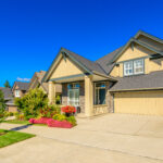 Large two-story suburban home with a two-car garage, landscaped front yard, and colorful flower beds.