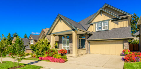 Large two-story suburban home with a two-car garage, landscaped front yard, and colorful flower beds.