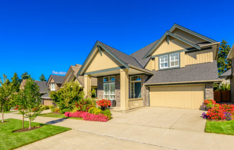 Large two-story suburban home with a two-car garage, landscaped front yard, and colorful flower beds.