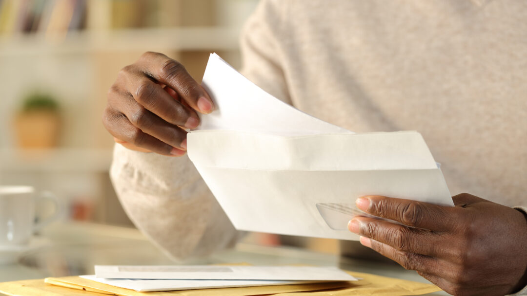 Person removing a letter from an envelope while sorting through mail at home.