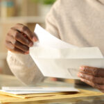 Person removing a letter from an envelope while sorting through mail at home.