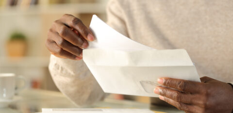 Person removing a letter from an envelope while sorting through mail at home.