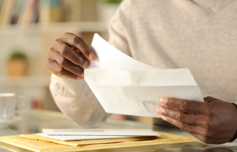 Person removing a letter from an envelope while sorting through mail at home.
