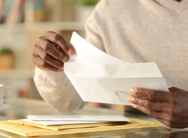 Person removing a letter from an envelope while sorting through mail at home.