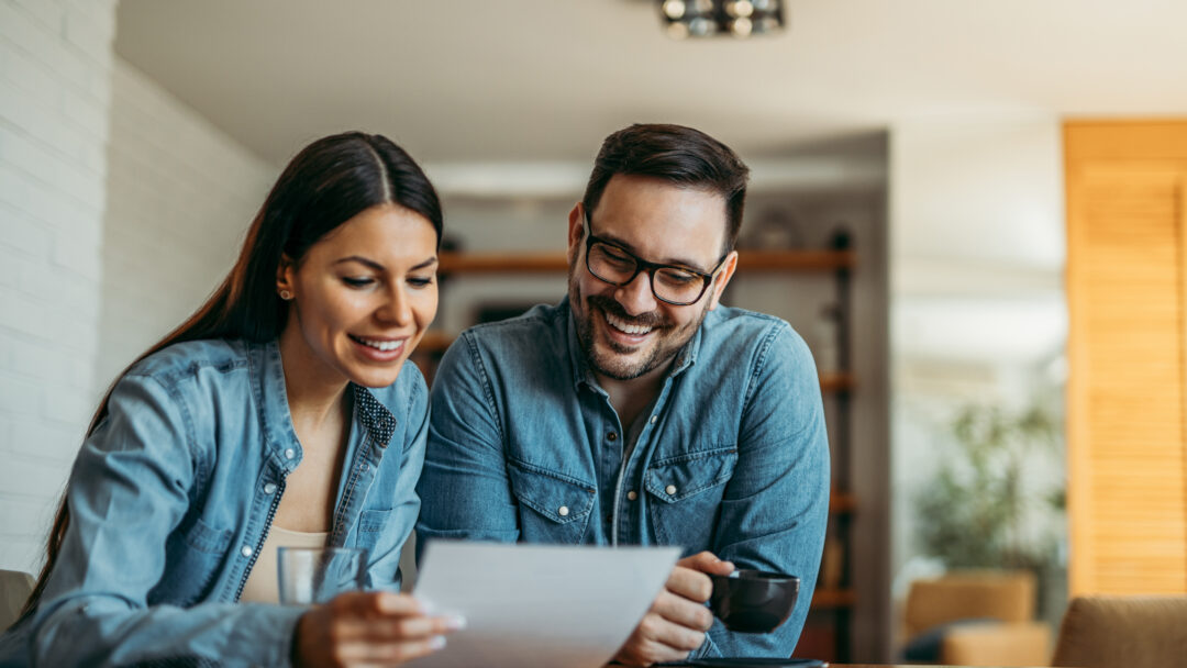 Couple smiling while reviewing paperwork together at a table at home.