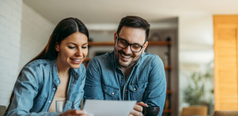 Couple smiling while reviewing paperwork together at a table at home.