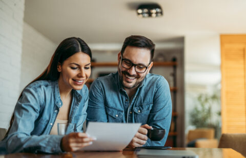Couple smiling while reviewing paperwork together at a table at home.
