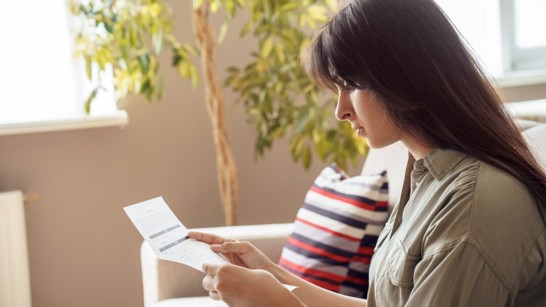 Woman sitting at home and reviewing a financial document.