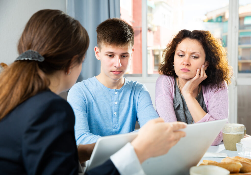 Mother and teenage son reviewing documents with an adviser at a table.