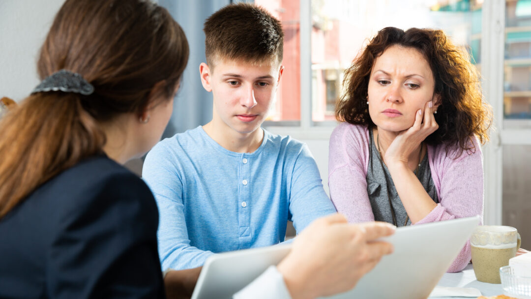 Mother and teenage son reviewing documents with an adviser at a table.