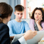 Mother and teenage son reviewing documents with an adviser at a table.