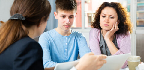 Mother and teenage son reviewing documents with an adviser at a table.