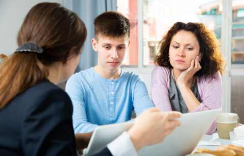 Mother and teenage son reviewing documents with an adviser at a table.
