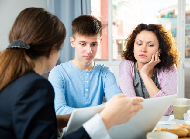Mother and teenage son reviewing documents with an adviser at a table.
