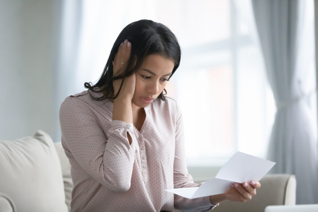 Woman looking worried while reading a letter at home.