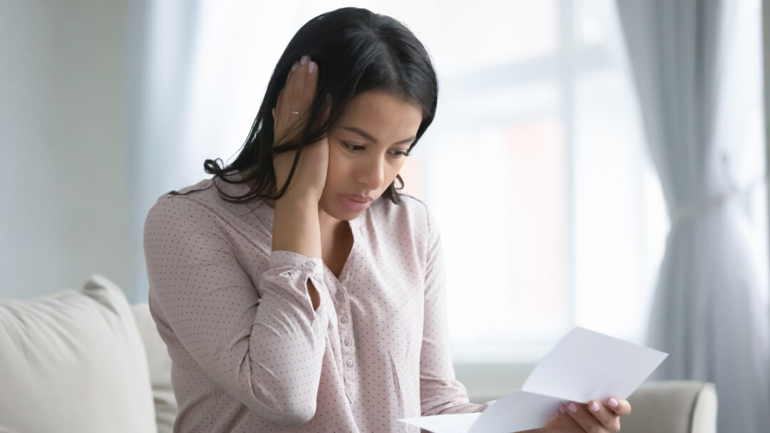 Woman looking worried while reading a letter at home.