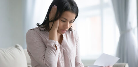 Woman looking worried while reading a letter at home.