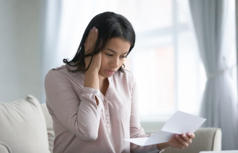 Woman looking worried while reading a letter at home.