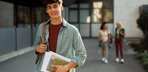 College student carrying books and a backpack while standing outside on campus.