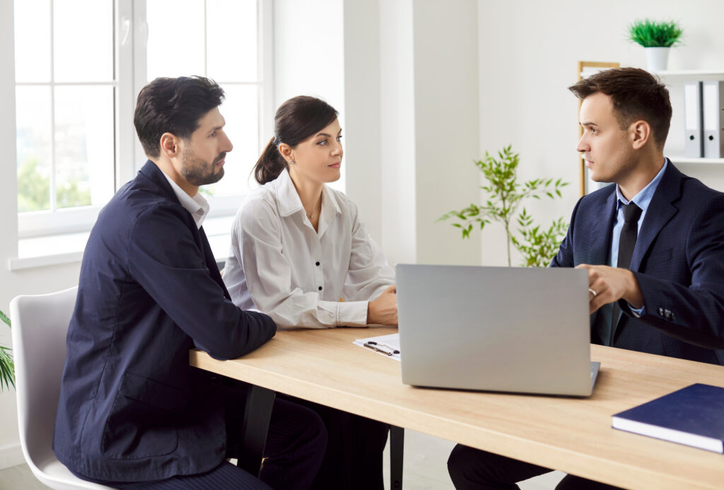 Couple sitting at a desk listening to a loan officer with a laptop in an office.