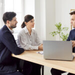 Couple sitting at a desk listening to a loan officer with a laptop in an office.
