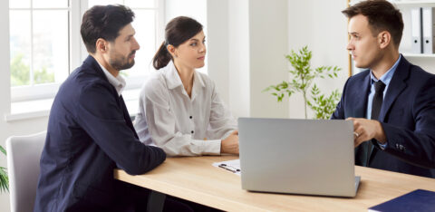 Couple sitting at a desk listening to a loan officer with a laptop in an office.