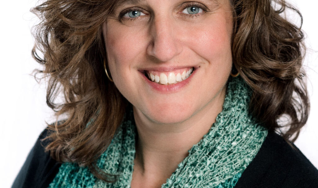 Smiling woman with shoulder-length brown hair wearing a green scarf against a white background.