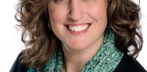 Smiling woman with shoulder-length brown hair wearing a green scarf against a white background.
