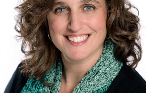 Smiling woman with shoulder-length brown hair wearing a green scarf against a white background.
