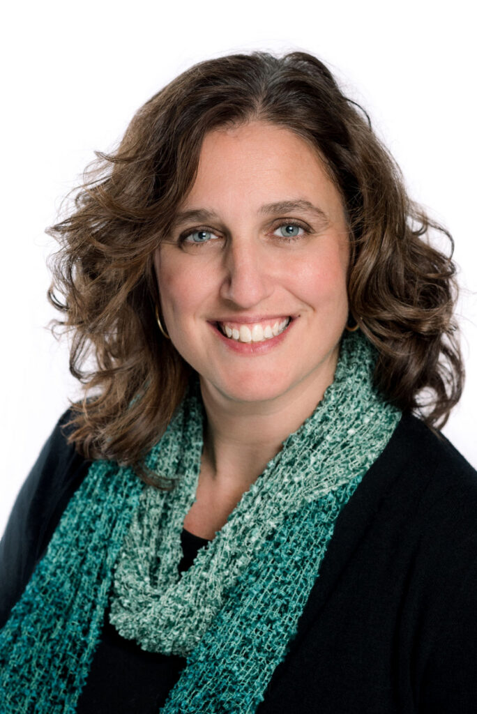 Smiling woman with shoulder-length brown hair wearing a green scarf against a white background.